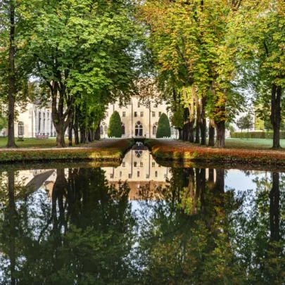 Un chemin bord&eacute; d'arbres avec le B&acirc;timent des moines Abbaye de Royaumont se refl&eacute;tant dans un &eacute;tang, entour&eacute; de feuillages d'automne.