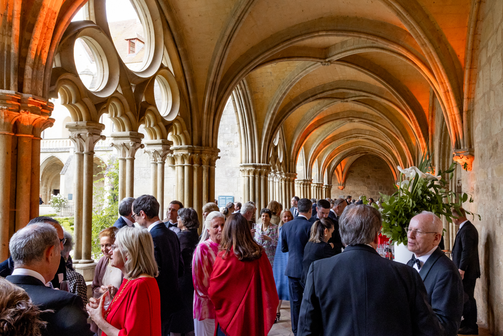 Des personnes en tenue de soirée se mêlent dans un cloître historique aux plafonds voûtés et aux colonnes de pierre de la Fondation Royaumont, un lieu connu pour ses prestigieux événements du Campus Royaumont et ses rassemblements de lauréats distingués.